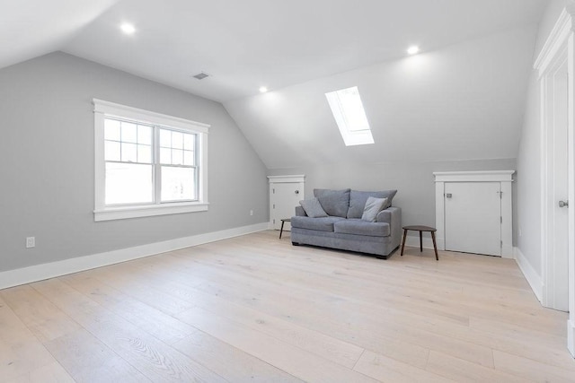 living area featuring lofted ceiling with skylight, light wood-style flooring, visible vents, and baseboards