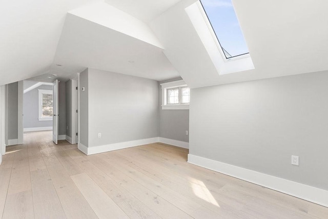 bonus room with lofted ceiling with skylight, light wood-type flooring, and baseboards