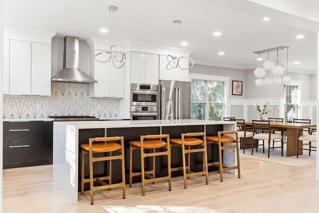 kitchen featuring a center island with sink, modern cabinets, stainless steel appliances, crown molding, and wall chimney range hood