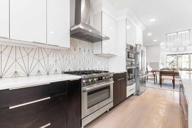 kitchen featuring wall chimney range hood, modern cabinets, stainless steel appliances, and light countertops