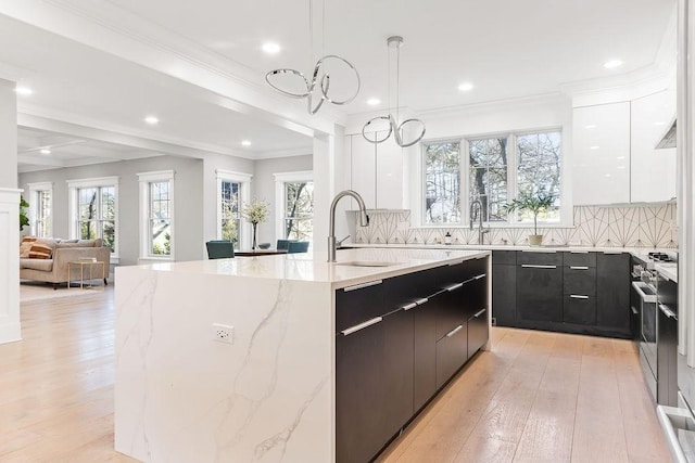 kitchen with stainless steel range, light wood-style floors, white cabinets, an island with sink, and modern cabinets