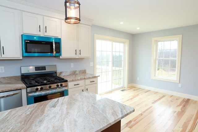 kitchen with a healthy amount of sunlight, light stone countertops, white cabinetry, and stainless steel appliances