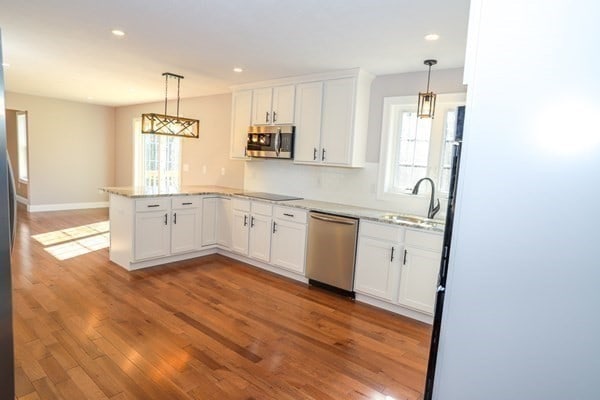 kitchen with white cabinets, kitchen peninsula, stainless steel appliances, and hanging light fixtures