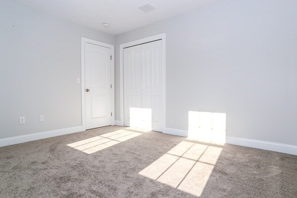 unfurnished bedroom with light colored carpet and a closet