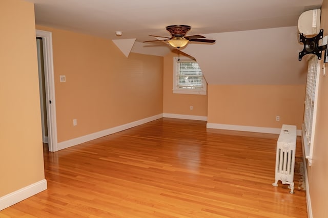 additional living space with light wood-type flooring, vaulted ceiling, radiator, and ceiling fan