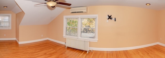 additional living space featuring an AC wall unit, a wealth of natural light, radiator heating unit, and wood-type flooring