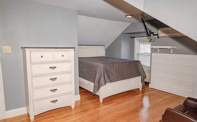 bedroom with radiator, light hardwood / wood-style flooring, a wall mounted air conditioner, and vaulted ceiling