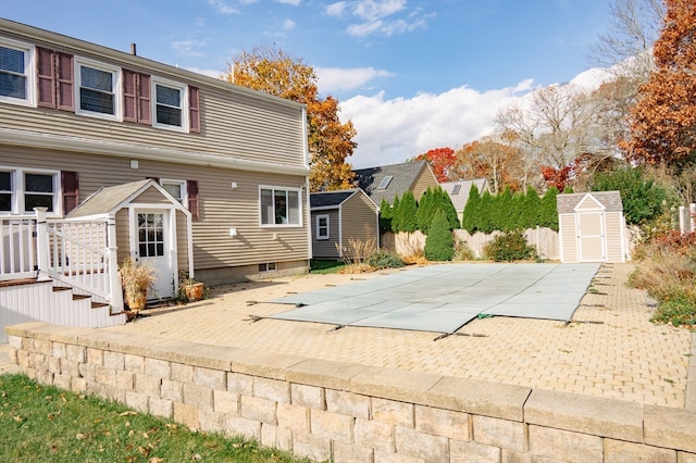 rear view of property featuring a patio area, a shed, and a covered pool