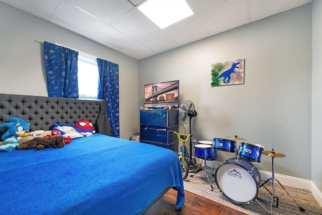 bedroom featuring baseboards, a drop ceiling, and wood finished floors