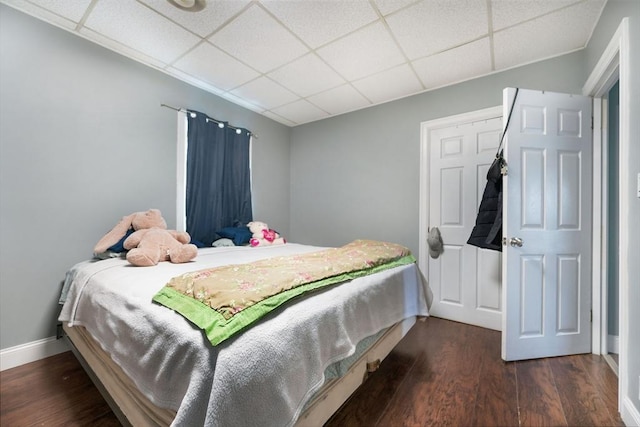 bedroom featuring baseboards, a drop ceiling, and wood finished floors