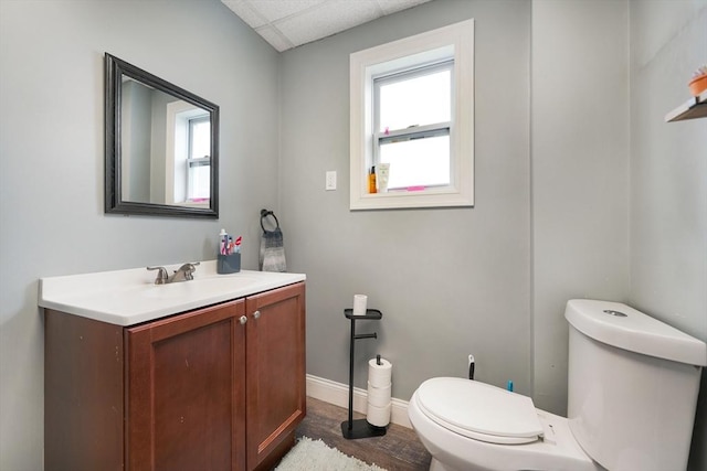 half bath with vanity, a drop ceiling, a wealth of natural light, and toilet