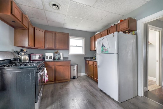 kitchen featuring brown cabinetry, freestanding refrigerator, wood finished floors, a paneled ceiling, and gas stove