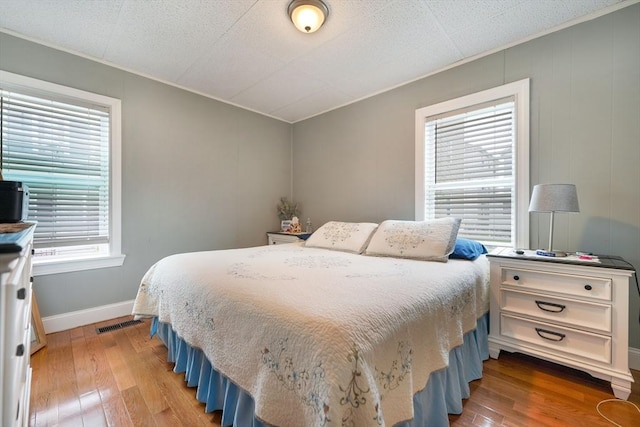 bedroom with light wood-style floors, baseboards, crown molding, and visible vents