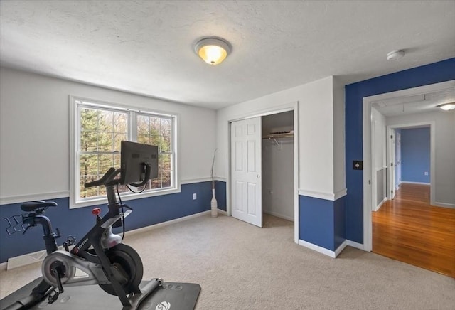 workout area featuring carpet flooring, a textured ceiling, and baseboards