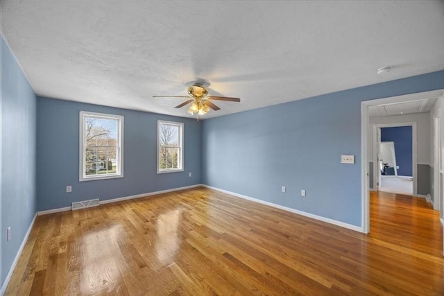 spare room with visible vents, wood finished floors, baseboards, attic access, and ceiling fan
