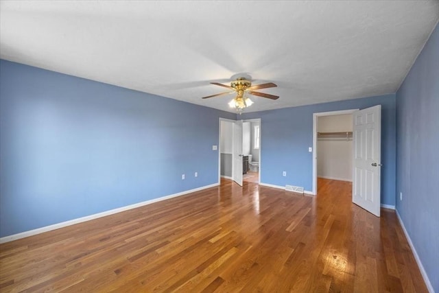 unfurnished bedroom featuring visible vents, wood finished floors, baseboards, a closet, and a spacious closet