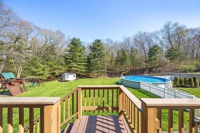 deck with a lawn, an outbuilding, a fenced in pool, a shed, and a playground