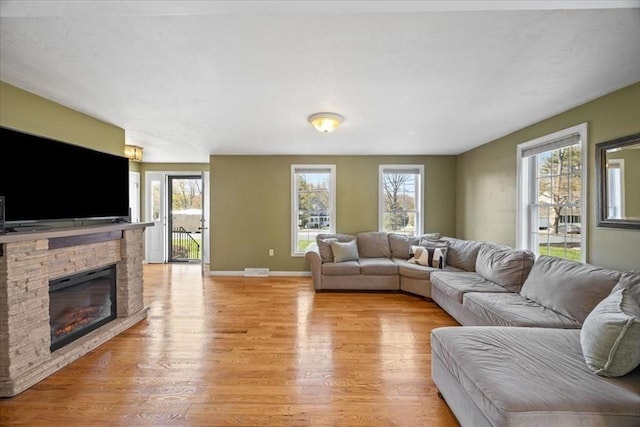 living room featuring baseboards, a stone fireplace, a wealth of natural light, and light wood finished floors