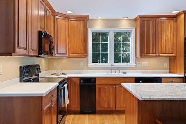 kitchen with brown cabinetry, black appliances, and a sink