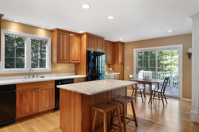 kitchen featuring brown cabinetry, light wood finished floors, a sink, black appliances, and a kitchen bar