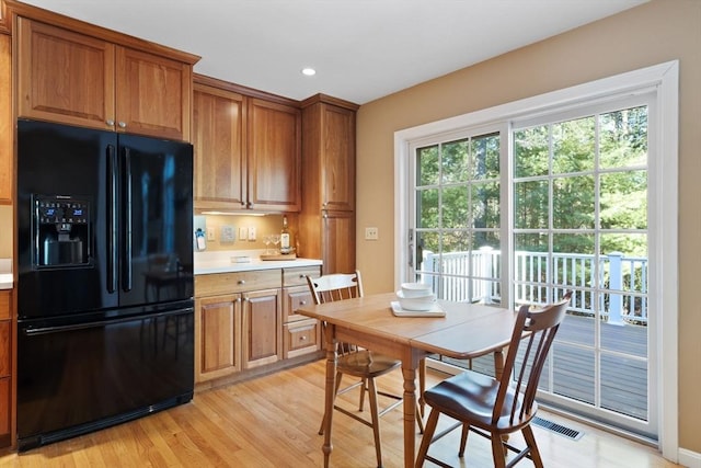 kitchen with light wood-type flooring, light countertops, recessed lighting, brown cabinetry, and black fridge with ice dispenser