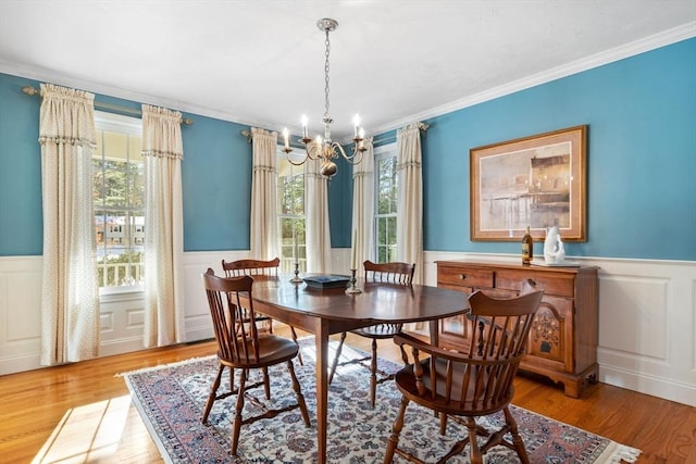 dining area featuring crown molding, a notable chandelier, wood finished floors, and a wainscoted wall