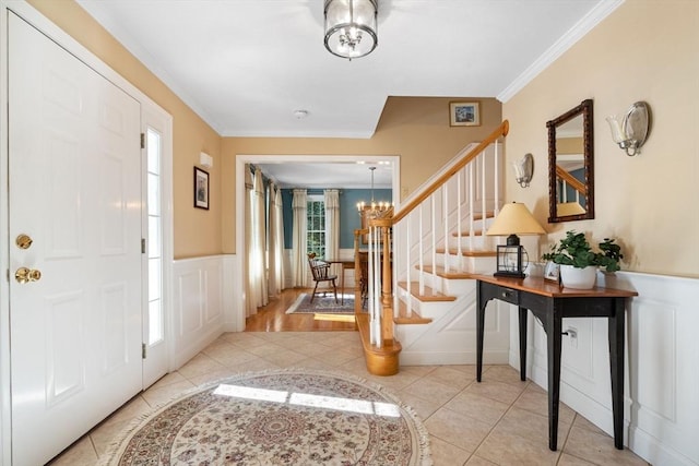 tiled entryway with a wainscoted wall, stairway, crown molding, a decorative wall, and a chandelier