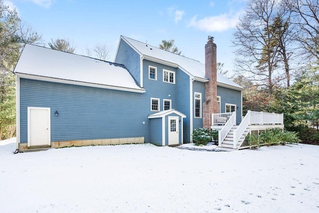 snow covered back of property with a deck, stairway, and a chimney