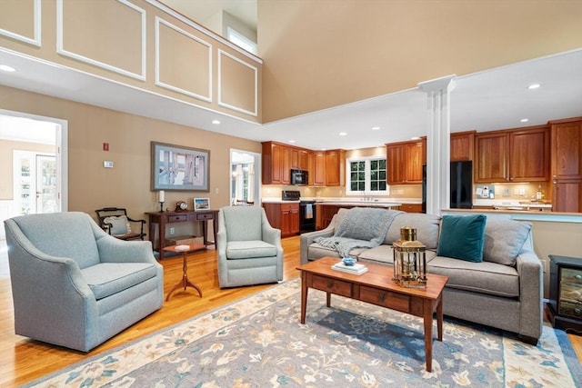 living area featuring recessed lighting, light wood-style floors, ornate columns, and a towering ceiling