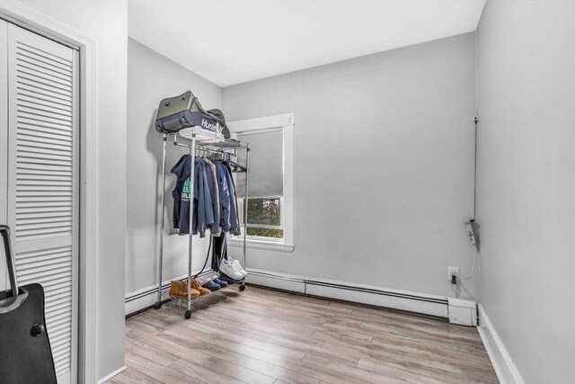 clothes washing area with baseboards, baseboard heating, and wood finished floors