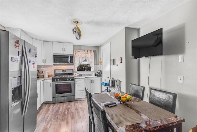 kitchen featuring stainless steel appliances, a textured ceiling, light wood-style flooring, backsplash, and light countertops