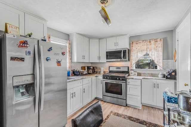 kitchen with a textured ceiling, decorative backsplash, light wood-style floors, stainless steel appliances, and white cabinets