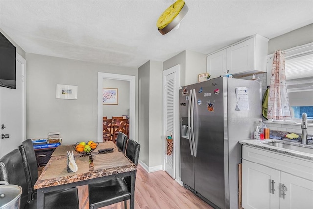 kitchen with light stone countertops, light wood finished floors, a sink, white cabinetry, and stainless steel fridge with ice dispenser