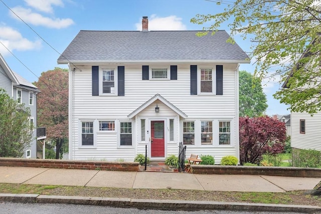 colonial inspired home featuring a chimney and roof with shingles