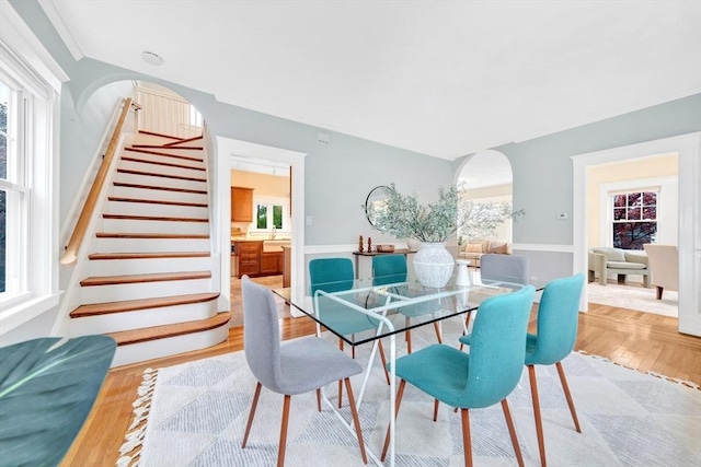 dining space with arched walkways, stairway, and wood finished floors
