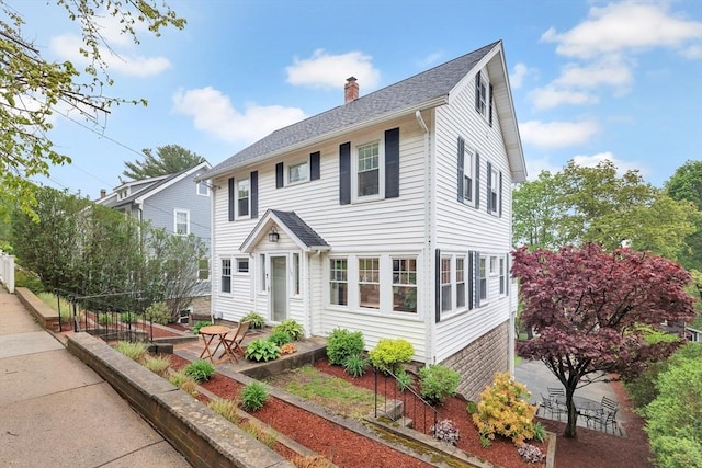 colonial home with a chimney, a patio, and roof with shingles