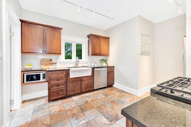 kitchen with rail lighting, appliances with stainless steel finishes, a sink, baseboards, and tasteful backsplash