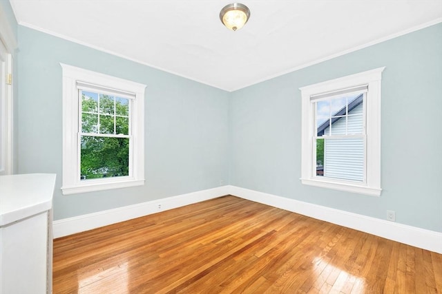 empty room featuring light wood-type flooring, crown molding, and baseboards