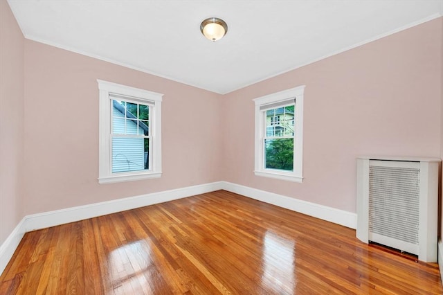 empty room featuring plenty of natural light, wood finished floors, baseboards, ornamental molding, and radiator heating unit