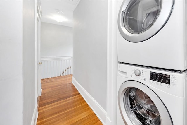 laundry room with stacked washer and clothes dryer, light wood-style floors, and baseboards