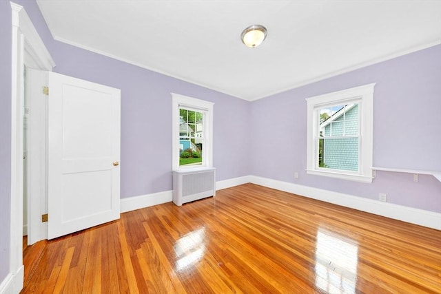 spare room with radiator, healthy amount of natural light, light wood-type flooring, baseboards, and crown molding