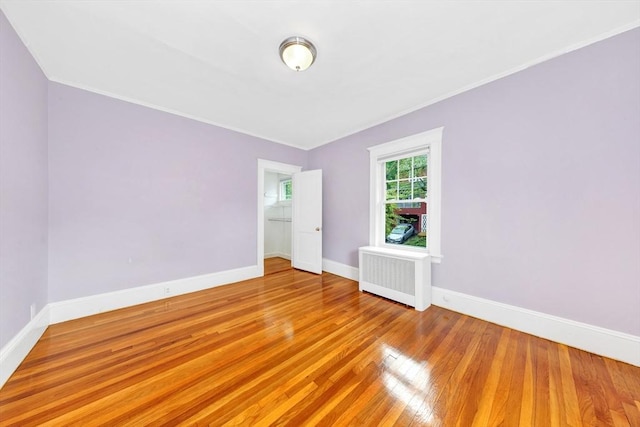 empty room with radiator heating unit, wood-type flooring, baseboards, and ornamental molding