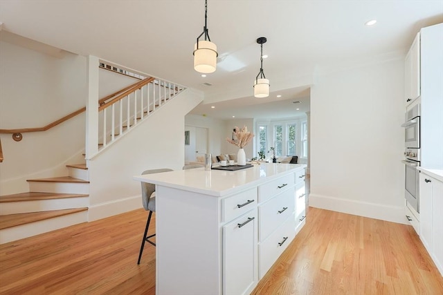 179 Main Unit 2, Medford, MA 02155 - kitchen with light wood-style floors, white cabinetry, a breakfast bar, pendant lighting, and a center island