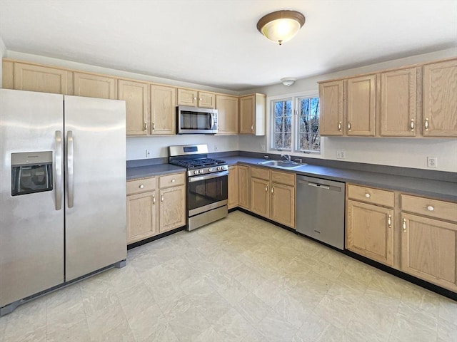 kitchen featuring dark countertops, light brown cabinetry, light floors, appliances with stainless steel finishes, and a sink