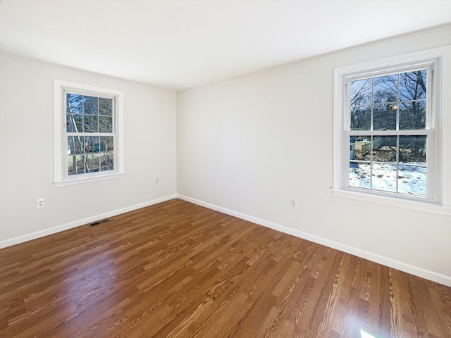 spare room with wood finished floors, plenty of natural light, visible vents, and baseboards