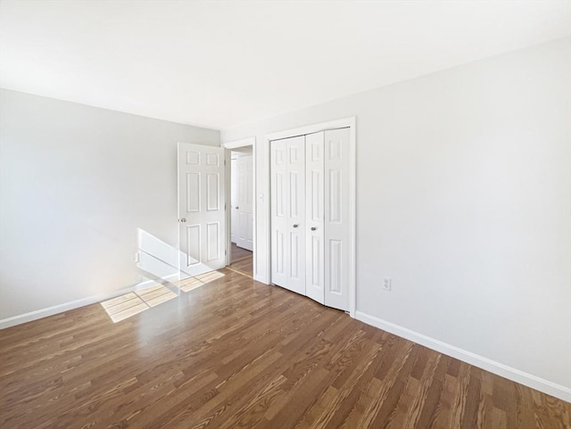 unfurnished bedroom with wood finished floors, baseboards, and a closet