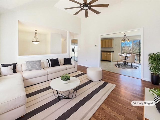 living area with ceiling fan with notable chandelier, a high ceiling, baseboards, and wood finished floors