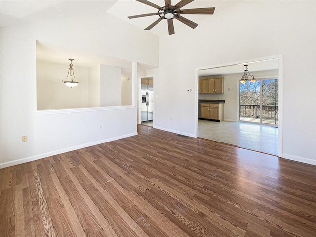 unfurnished living room with baseboards, dark wood-style floors, and ceiling fan with notable chandelier