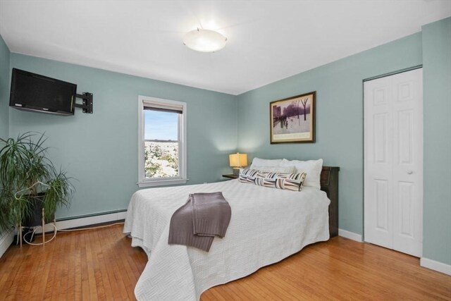 bedroom with a baseboard heating unit, wood finished floors, and baseboards