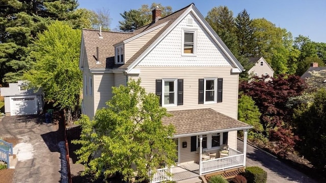 rear view of property featuring an outdoor structure, covered porch, a garage, driveway, and a chimney